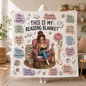 Puede incluir: Una manta con capucha blanca con el texto 'THIS IS MY READING BLANKET' y 'Emma'. El diseño muestra a una persona sentada en un sillón rosa leyendo un libro con un gato, pilas de libros, una flor y varias citas relacionadas con la lectura.