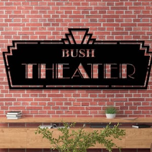 May include: Black metal sign with an art deco design. The sign reads "Bush Theater".