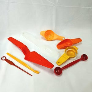 Könnte beinhalten: Eine Sammlung von Küchenutensilien, bestehend aus einem roten Tortenheber, einem weißen Teigschaber, einem gelben Eiertrenner, einem roten Doppelmesslöffel, einer orangefarbenen Zitruspresse, einer orangefarbenen Schaufel und einem gelben Werkzeug.