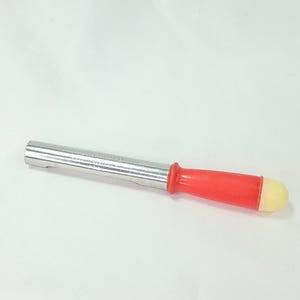 May include: A kitchen apple corer featuring a cylindrical stainless steel blade with a serrated edge, a bright red plastic handle, and a rounded off-white end cap. The metal shaft is smooth and reflects light, while the handle is contoured.