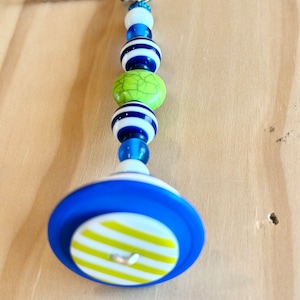Pode incluir: Um puxador de ventilador listrado azul e branco com uma conta verde e branca e uma conta listrada azul e branca. O puxador do ventilador está preso a uma corrente prateada.