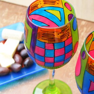 Pode incluir: Duas taças de vinho coloridas com desenhos geométricos abstratos pintados nelas. As taças estão cheias de padrões coloridos em tons de azul, verde, rosa, laranja e amarelo.