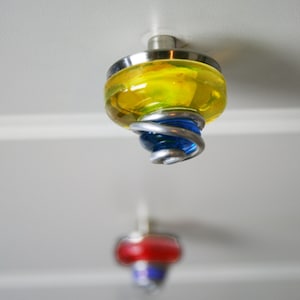 May include: A yellow glass cabinet knob with a blue glass accent and a silver metal swirl design.