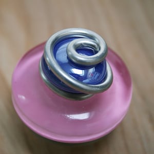 May include: A pink glass base with a blue glass sphere wrapped in silver wire. The sphere is a decorative element.