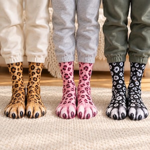 Puede incluir: Tres pares de calcetines con estampados realistas de patas de animales. El primer par tiene un patrón de leopardo amarillo y negro, el segundo un patrón de leopardo rosa y negro, y el tercero un patrón de manchas blancas y negras con dedos oscuros.