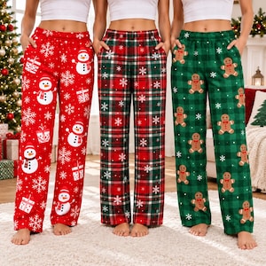 May include: Three pairs of pajama pants with elastic waistbands. The first pair is red with white snowmen and gift boxes. The second pair features a red, green, and white plaid pattern with white snowflakes. The third is green plaid with gingerbread men.
