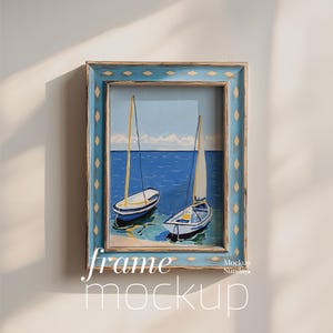 Puede incluir: Un marco de madera azul con un borde blanco y amarillo rodea una pintura de dos veleros en una masa de agua azul. La pintura se titula "frame mockup".