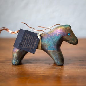 May include: A handcrafted ceramic Spirit Pony figurine with iridescent colours, copper wire mane, and a turquoise eye. A black tag is attached with the text "Spirit Pony". The figurine is displayed on a wooden surface.