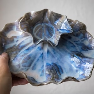 May include: A ceramic serving dish set with a leaf design. The set includes a large, shallow dish and a smaller, bowl-shaped dish. The dishes feature a blue and white glaze with brown accents, creating a unique, artistic look.