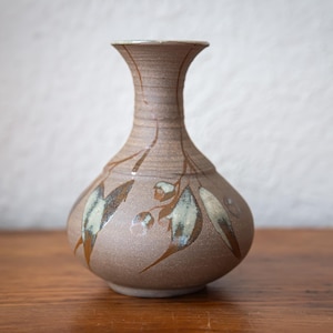 May include: A light brown ceramic vase with a rounded body and a narrow neck. The surface features a textured finish with hand-painted botanical motifs in shades of dark brown, cream, and muted green, depicting leaves and small buds.