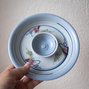 May include: A handmade ceramic serving dish with a pale blue rim and a central dip bowl. The dish has a white interior with blue and red abstract floral designs. The dip bowl is pale blue with a spiral design.