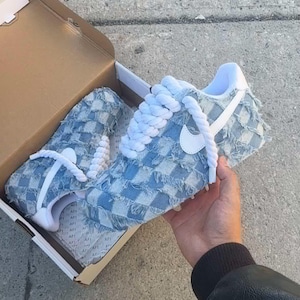 May include: A pair of light blue denim sneakers with white laces and a white Nike swoosh. The sneakers have a checkered pattern and frayed edges.