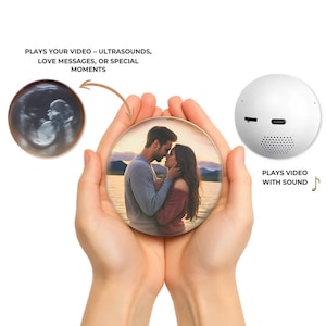 Può includere: Un dispositivo sferico bianco con un altoparlante e porte, accanto a una foto rotonda con una coppia che si bacia. La foto è tenuta in mano. Il testo recita "PLAYS YOUR VIDEO - ULTRASOUNDS, LOVE MESSAGES, OR SPECIAL MOMENTS" e "PLAYS VIDEO WITH SOUND".