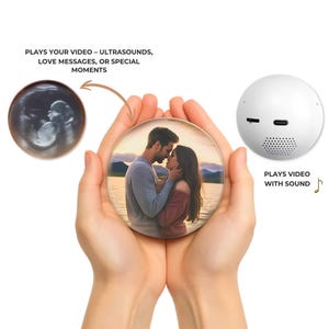 May include: A white, spherical video player with a speaker and ports, next to a round photo with a couple kissing. An ultrasound image is also shown. Text reads: "PLAYS YOUR VIDEO - ULTRASOUNDS, LOVE MESSAGES, OR SPECIAL MOMENTS" and "PLAYS VIDEO WITH SOUND".