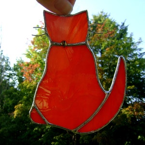 May include: A stained glass cat figurine with a bright orange body and silver accents. The cat is facing to the right and has a long tail.