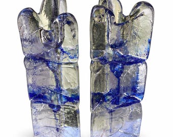 May include: Two tall, vertical glass sculptures featuring a clear, textured surface with internal streaks of deep blue pigment. Each piece has an irregular, organic top edge and a rectangular base, with light reflecting through the translucent material.