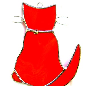 May include: A red stained glass cat ornament with a silver bell on its belly.
