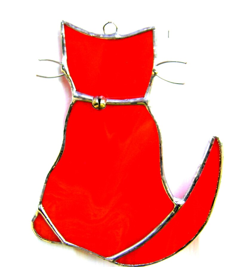 May include: A red stained glass cat ornament with a silver bell on its belly.