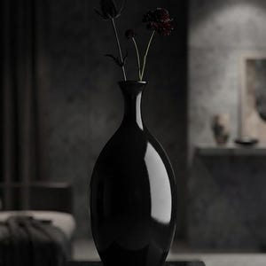 May include: A tall, smooth, black ceramic vase with a rounded, bulbous body and a slender neck. The vase contains two dark, dried flower stems, one featuring a spiky thistle-like head and the other a small, deep purple, rounded blossom.