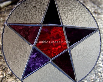 May include: A stained glass window featuring a five-pointed star with red, purple, and black glass pieces. The star is set against a white background. The text "Gothic Glass Studio" is visible in the center of the star.