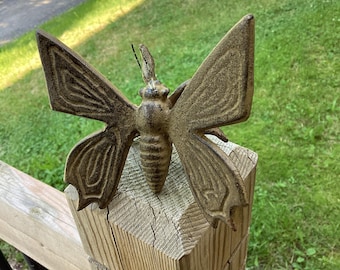 May include: A cast iron butterfly garden stake with a rustic brown finish. The butterfly is perched on a wooden post.