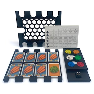 May include: A black game board with a grid of hexagonal spaces, a set of cards with numbers and carrots, a set of colored tokens, and a die. The cards are labeled with numbers 1, 3, 5, 10, 15, 30, and 60. The tokens are labeled with different animal symbols. The game board has a black plastic frame.