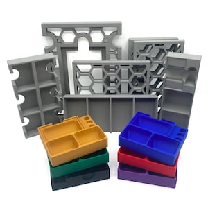 Puede incluir: Un conjunto de organizadores de plástico gris con un patrón de panal. Los organizadores están apilados uno encima del otro. También hay cinco organizadores más pequeños en diferentes colores: amarillo, verde, negro, rojo y morado.
