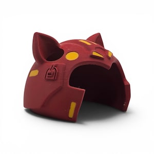 May include: A red cat-eared helmet with yellow accents. The helmet has a rounded shape with ear-like protrusions on top and yellow circular and rectangular details. The helmet is made of a solid material and is likely a costume piece.