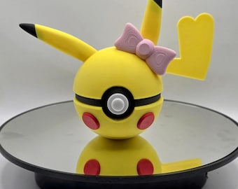May include: A yellow Pikachu-inspired figurine with a pink bow, red cheek circles, and black accents. The figure is displayed on a reflective surface, showcasing its design and details. The figurine's ears and tail are also yellow with black tips.