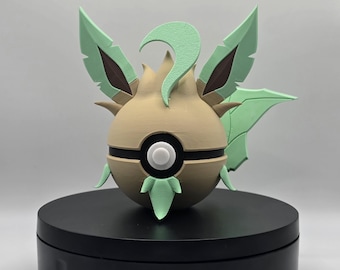 May include: A 3D printed figurine of a Pokemon character, resembling a brown and green ball with a white circle in the centre. The character has green leaf-like appendages and a green crest on its head.
