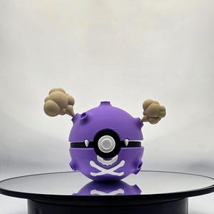 May include: A purple and white 3D printed Pokemon figure of a Koffing with a skull and crossbones design. The figure is on a black rotating display stand.