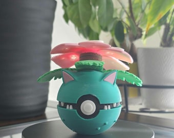 May include: A green and pink 3D printed Pokemon figure of a Venusaur. The figure is posed with its mouth open and its flower on top of its head.