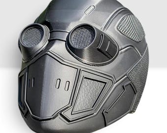May include: A matte black full-face mask featuring two prominent circular eye openings with mesh coverings, a structured nose section with vertical ventilation slits, and textured side panels with a geometric pattern across the surface.