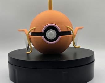 Könnte beinhalten: Eine orangefarbene und weiße Magikarp-Figur, eine Figur aus der Pokémon-Franchise. Die Figur hat einen runden Körper mit einem schwarzen Streifen und rosa und weißen Akzenten. Sie hat gelbe Flossen und eine gelbe Rückenflosse. Die Figur wird auf einem schwarzen Drehständer präsentiert.