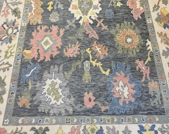 May include: A rectangular area rug with a dark gray center and a cream-colored border. The rug features a floral pattern in shades of pink, blue, orange, and yellow. The border has a repeating floral design. The rug is suitable for a living room or bedroom.