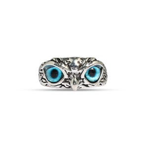 May include: A silver-colored ring shaped like an owl's head, featuring bright blue eyes. The ring has detailed feather-like textures and a small beak. The owl ring is a unique piece of jewelry.