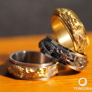 May include: Three metal rings with dragon designs. One ring is gold-colored, another is silver-colored, and the third is a combination of gold and silver. The rings are stacked on top of each other, showcasing the intricate details of the dragon carvings.