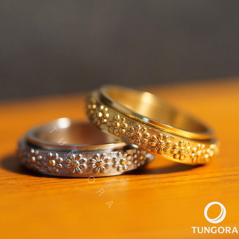 Gold daisy flower spinner ring with embossed floral design, reflecting warm light on a wooden background. Boho meditation jewelry, flower fidget ring for women, calming spinner ring, stress relief gift, gold floral band for mindfulness and focus.