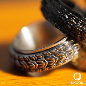 May include: Close-up of two silver rings with intricate, textured patterns. One ring is in sharp focus, revealing a detailed design, while the other is slightly blurred. The rings are set against a warm, orange background.