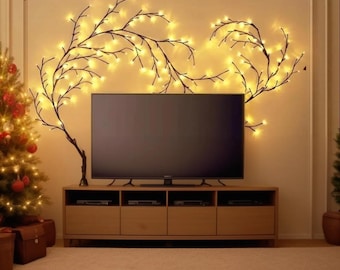 May include: A living room with a TV above a wooden cabinet. The wall is decorated with branches and warm white fairy lights. A Christmas tree with decorations is on the left. The room has a warm, inviting atmosphere.