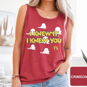 May include: A crimson sleeveless tank top featuring a graphic print of white clouds and the yellow text "I KNEW IT, I KNEW YOU" with a red heart containing the letters "TS" positioned below the text on the front of the garment.