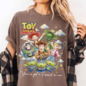 May include: Brown t-shirt featuring a colorful graphic of Toy Story characters, including Woody, Buzz Lightyear, and the Little Green Men. The words "TOY STORY" and "You've got a Friend in me" are also displayed.