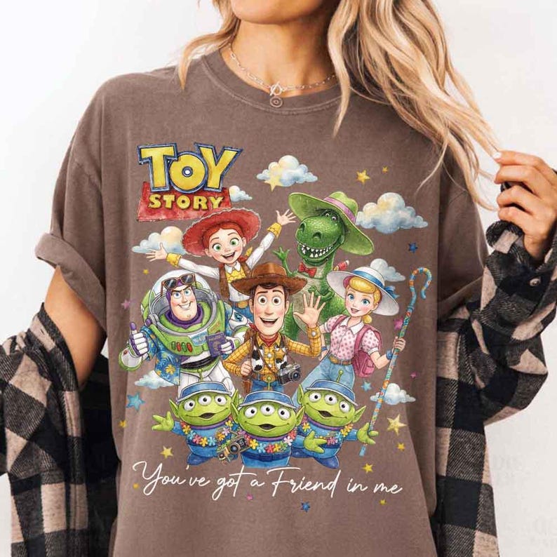May include: Brown t-shirt featuring a colorful graphic of Toy Story characters, including Woody, Buzz Lightyear, and the Little Green Men. The words "TOY STORY" and "You've got a Friend in me" are also displayed.