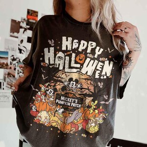May include: Dark gray t-shirt with a Halloween-themed graphic. The design features the text "Happy Halloween" above a scene with Mickey Mouse and friends in a pumpkin patch. Bats and other Halloween elements are also included.