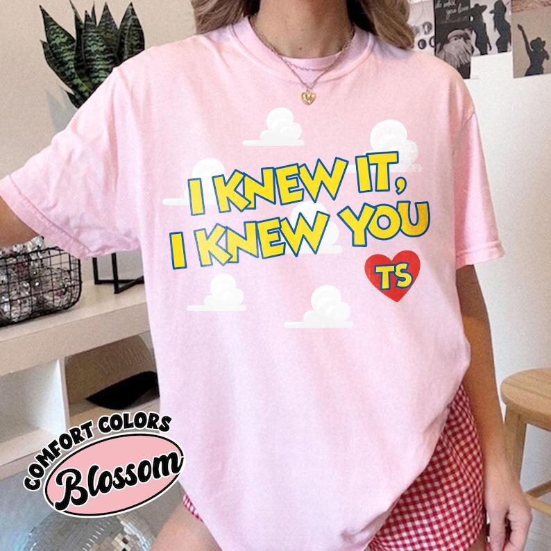 Może przedstawiać: Jasnor&oacute;żowy t-shirt z kr&oacute;tkim rękawem z nadrukiem białych chmur i ż&oacute;łtym napisem I KNEW IT, I KNEW YOU. Pod tekstem znajduje się czerwone serce z literami TS. Koszulka posiada okrągły dekolt oraz luźny kr&oacute;j, zapewniający swobodę noszenia na co dzień.