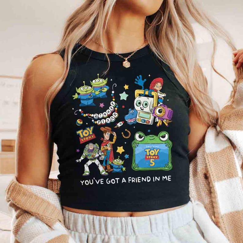 K&ouml;nnte beinhalten: Ein schwarzes &auml;rmelloses Tanktop mit einem bunten Grafikdruck von Toy Story-Figuren wie Woody, Buzz Lightyear und Aliens. Das Design enth&auml;lt den Text Toy Story 5 sowie den Schriftzug YOU'VE GOT A FRIEND IN ME in wei&szlig;en Buchstaben.