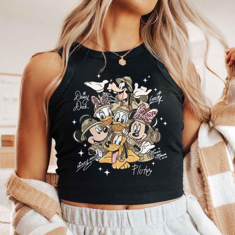 Pu&ograve; includere: Canotta nera con una grafica dei personaggi Disney Topolino, Minnie, Paperino, Paperina, Pippo e Pluto. I personaggi indossano cappelli da safari. I nomi dei personaggi sono scritti in corsivo. La canotta &egrave; senza maniche.