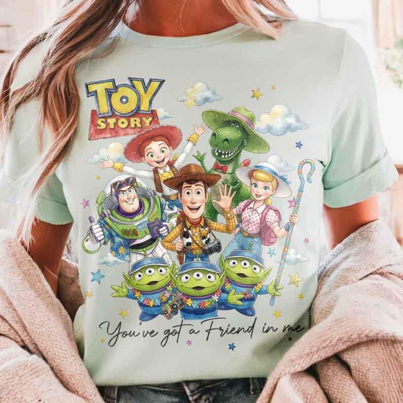May include: Light blue t-shirt featuring a colorful graphic of Toy Story characters, including Woody, Buzz Lightyear, and the Little Green Men. The text "Toy Story" is at the top, and "You've got a Friend in me" is at the bottom.