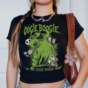 May include: Black crop top featuring a green graphic of Oogie Boogie from The Nightmare Before Christmas. The text "Oogie Boogie" and "I'm the Oogie Boogie Man!" are printed in green. The shirt has short sleeves.