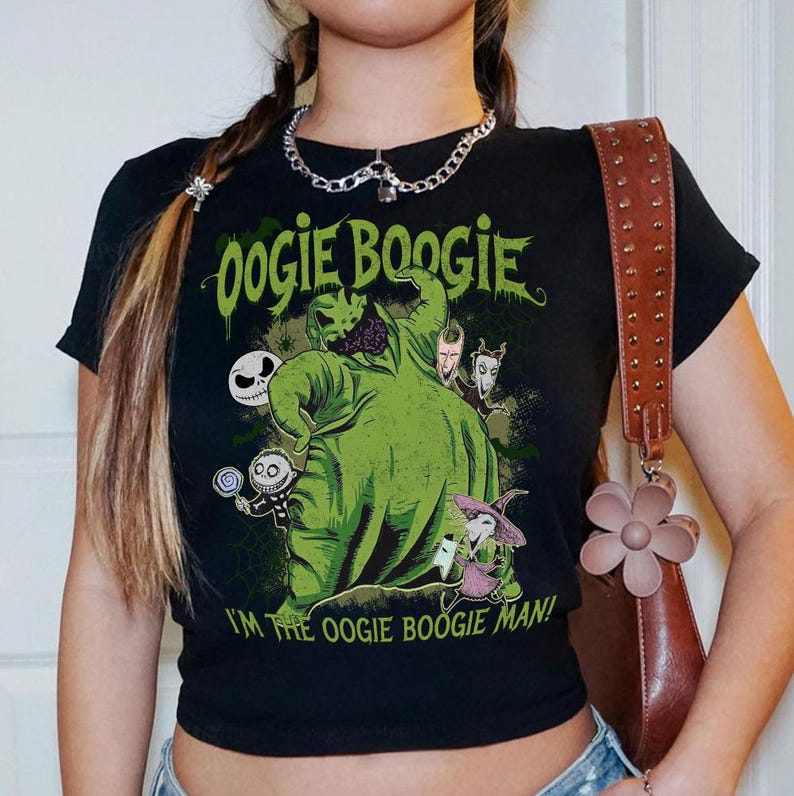 May include: Black crop top featuring a green graphic of Oogie Boogie from The Nightmare Before Christmas. The text "Oogie Boogie" and "I'm the Oogie Boogie Man!" are printed in green. The shirt has short sleeves.